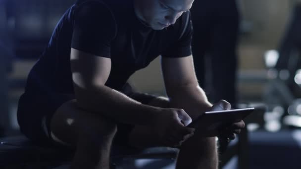 Hombre deportivo guapo ajuste está utilizando una tableta en el gimnasio . — Vídeos de Stock