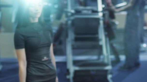 Ελκυστική fit σπορ κορίτσι σε μαύρα αθλητικά ρούχα ποζάρει με αλτήρα στο γυμναστήριο. — Αρχείο Βίντεο