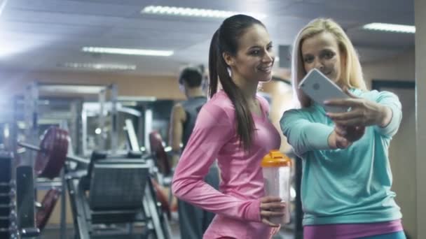 Twee aantrekkelijke fit sportieve meisjes maken selfie foto's op mobiele telefoon in de sportschool. — Stockvideo