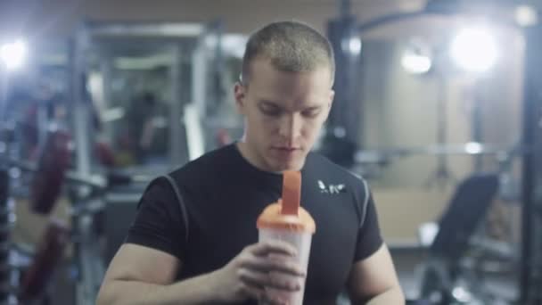 Hombre deportivo guapo en forma bebe de una coctelera y posa en el gimnasio . — Vídeos de Stock