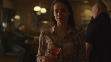 Mutlu çekici kız onun koltuk kalabalık bir barda bir içki ile yürüyor.