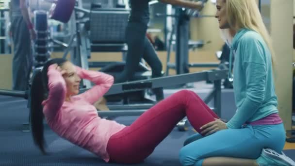 Atractiva chica deportiva en forma hace ejercicios abdominales en el gimnasio con la ayuda de un amigo . — Vídeo de stock
