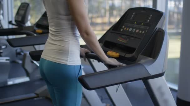 Attractive fit sporty girl is running on treadmill and listening to music in the gym. — Stock Video