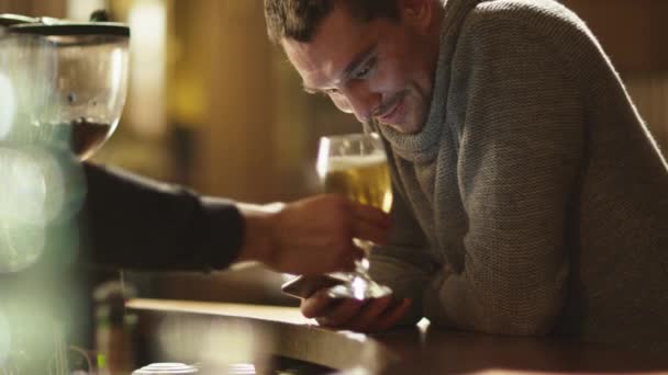 L'homme attrayant utilise un smartphone dans un bar pendant que le serveur lui apporte de la bière . — Video