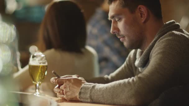Mannen är att skriva ett meddelande på en smartphone i en bar när ett glas öl står på räknaren. — Stockvideo