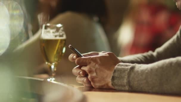 ビールのグラスはカウンターの上に立っている間男はバーでスマート フォンでメッセージを入力してください。. — ストック動画
