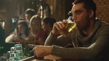 Çekici adam kalabalık bir barda lager bira içiyor.