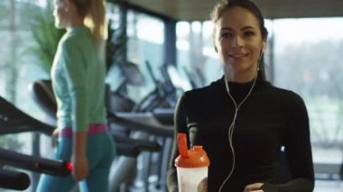 Çekici beyaz kız spor salonunda bir koşu bandı yanında bir protein shake içki içiyor.