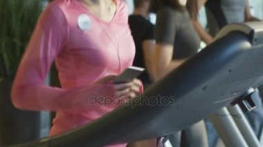 Kulaklık ile spor salonunda treadmill çalıştıran çekici beyaz kız ağır çekim görüntüleri.