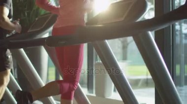 Telefon ve kulaklık ile spor salonunda treadmill çalıştıran çekici beyaz kız.