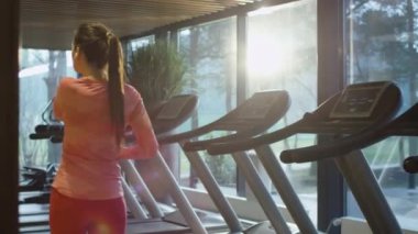 Çekici beyaz kız kulaklık ile bir boş spor salonunda treadmill üzerinde çalıştırmak başlıyor.