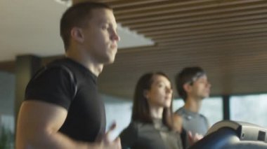 Egzersiz ve spor salonunda koşu bandı üzerinde çalışan kadın ve genç atletik erkek.