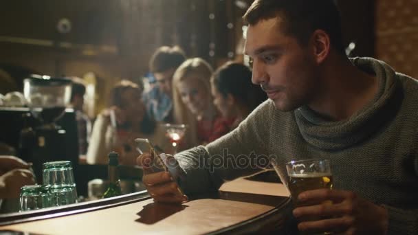 Happy man holds a glass of beer while using a smartphone in a bar. — Stock Video