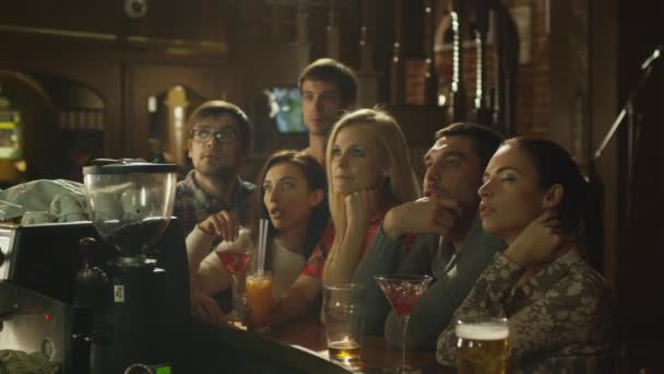 Amigos están sentados con bebidas y viendo un partido de deportes en un bar . — Vídeos de Stock