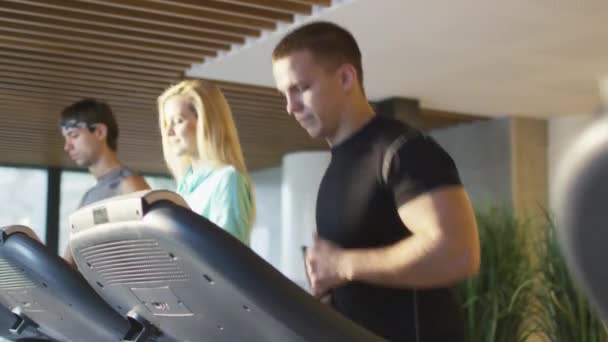 Egzersiz ve spor salonunda koşu bandı üzerinde çalışan kadın ve genç atletik erkek. — Stok video