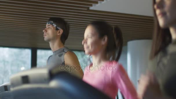 Slow motion footage of young athletic men and women exercising and running on treadmill in sport gym. — Stock Video