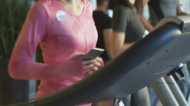 Slow motion beelden van aantrekkelijke Kaukasische meisje draait op de loopband in de sportschool sport met koptelefoon. — Stockvideo