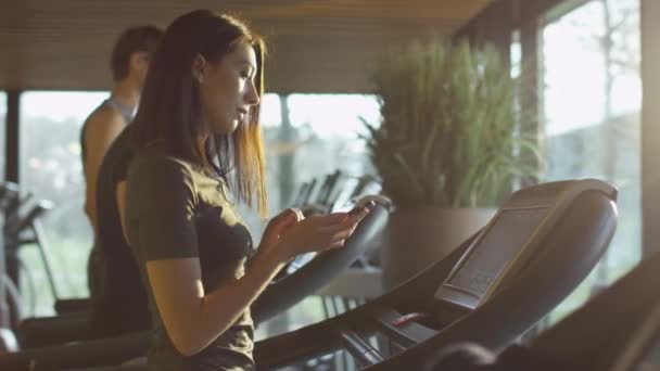 Attraente ragazza caucasica sta iniziando a correre sul tapis roulant nella palestra sportiva con auricolari . — Video Stock