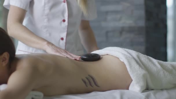 Молодая брюнетка получит расслабляющий каменный массаж в оздоровительном центре . — стоковое видео