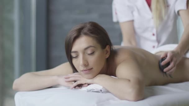 Junge brünette Frau bekommt eine entspannende Steinmassage im Wellness-Center. — Stockvideo