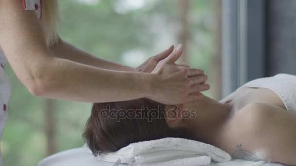 Jonge mooie vrouw krijgt een hoofd en gezicht massage in het wellnesscentrum. — Stockvideo