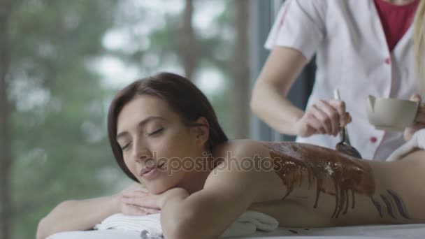 Jovem mulher bonita está recebendo um relaxante tratamento de massagem de chocolate no centro de bem-estar . — Vídeo de Stock