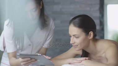 Kadın masör bir tablet bir müşteriye sağlık merkezinde dinlendirici bir yordam sırasında gösteriyor.