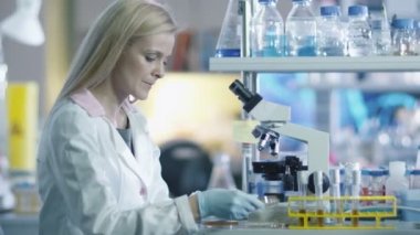 Sarışın kadın bilim adamı bir laboratuvar mikroskop üzerinde çalışıyor.