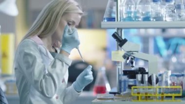 Sarışın kadın bilim adamı bir mikroskop örnek bir laboratuarda test etmek için hazırlanıyor.