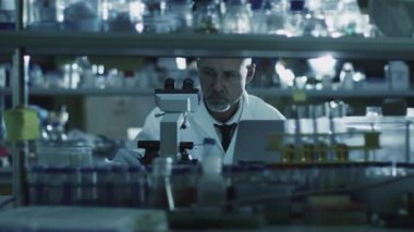 Yorgun üst düzey erkek bilim adamı bir laboratuvar mikroskop ile çalışma.