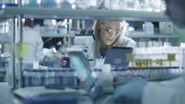 Kadın bilim adamı mikroskop ve bir tablet bir laboratuarda çalışırken kullanıyor.