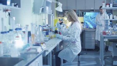 Kadın bilim adamı meslektaşları ile bir laboratuarda çalışırken bir mikro pipet kullanıyor.