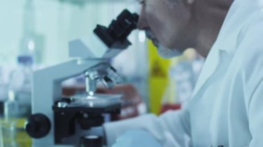 Üst düzey bilim adamı meslektaşları ile bir laboratuvar mikroskop ile çalışıyor.