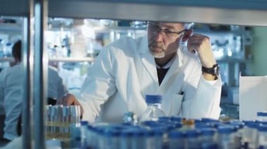 Üst düzey bilim adamı bir laboratuvar masasında oturan ve tüp örnekleri ile çalışma.