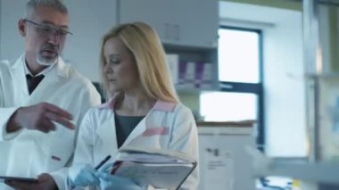 Kıdemli ve kağıtları ve tablet ile kadın bilim adamları yürüyüş ve bir laboratuvarda muhabbet. 