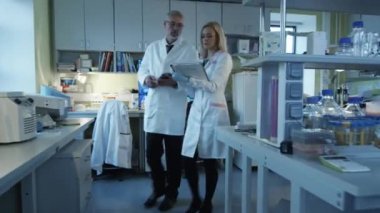 Kıdemli ve kağıtları ve tablet ile kadın bilim adamları yürüyüş ve bir laboratuvarda muhabbet. 