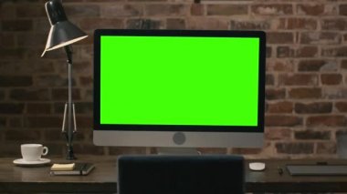Bir bilgisayar monitörü bir tablet, lamba, kahve fincanı, defter ve fare bir çatı katında yanındaki bir masada yeşil ekran konumu olan görüntüleri.