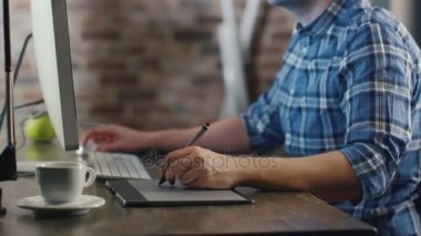 Bir çatı katında bir monitör önünde genç tasarımcı oturma ve bir grafik tablet üzerinde çizim.