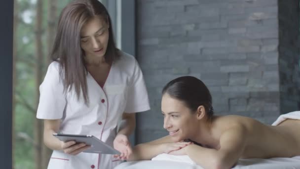 Masażysta kobieta pokazuje tablet do klienta podczas relaksu w centrum odnowy biologicznej. — Wideo stockowe