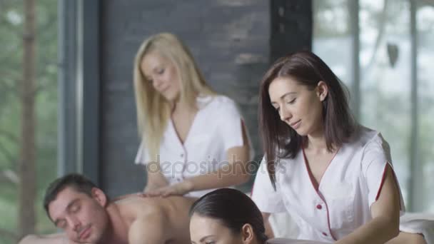 Młoda para jest coraz relaksujący masaż z kobiece masażystów w centrum odnowy biologicznej. — Wideo stockowe