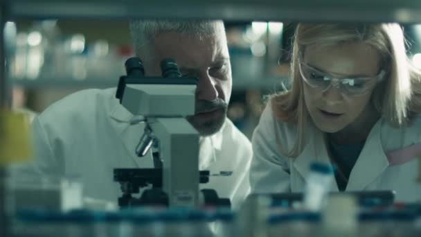 Homme et femme scientifiques travaillent avec un microscope et une tablette dans un laboratoire . — Video