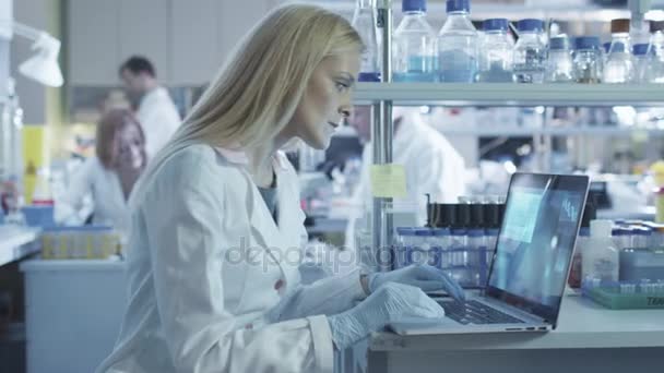 Científica femenina está utilizando una computadora portátil mientras trabaja en un laboratorio . — Vídeo de stock