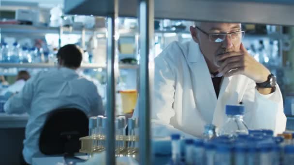 Ανώτερος επιστήμονας είναι κάθεται στο τραπέζι σε ένα εργαστήριο και να εργάζονται με σωλήνα δείγματα. — Αρχείο Βίντεο