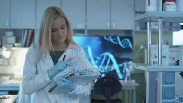 Mulher cientista está andando com documentos em um laboratório onde colegas estão trabalhando . — Vídeo de Stock