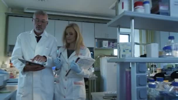 Des scientifiques seniors et féminines avec des papiers et des tablettes marchent et discutent dans un laboratoire . — Video