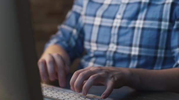 Joven en gafas está sentado frente a un monitor en un loft y trabajando . — Vídeos de Stock