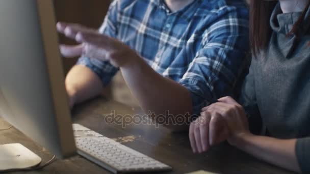 Joven hombre y mujer están trabajando en una computadora en un loft mientras discuten un proyecto . — Vídeos de Stock