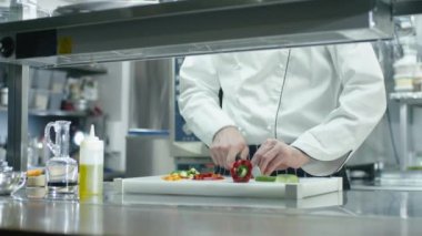 Restoranda ya da otelde ticari bir mutfakta profesyonel bir aşçı yeşil sebzeleri dilimliyor..