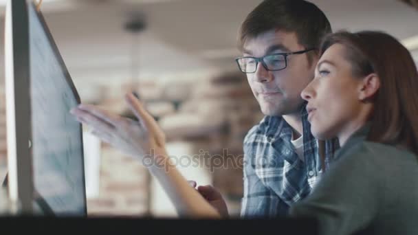 Fiatal férfi és nő dolgoznak egy számítógépen a padláson, miközben egy projektről beszélgetnek.. — Stock videók