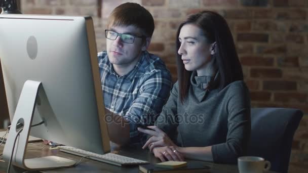Fiatal férfi és nő dolgozik egy számítógépen, miközben megvitatják a projekt. — Stock videók